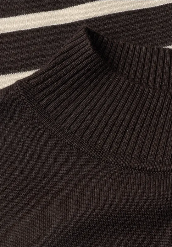 Schwarzer Rollkragenpullover mit geripptem Strickmuster, vor weiß-schwarz gestreiftem Hintergrund.