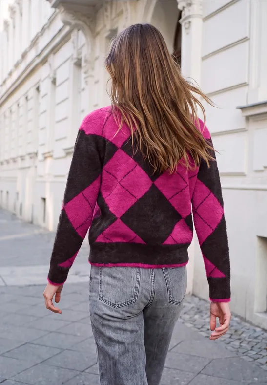 Frau von hinten in pink-schwarzem Rautensweater und grauen Jeans geht die Straße entlang.
