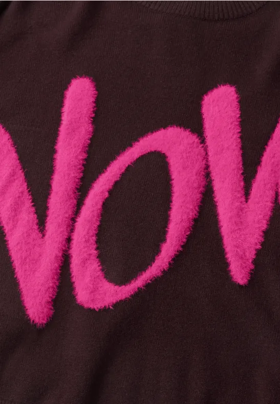 Pull marron avec lettres roses fluo en relief formant "VOV" sur la poitrine.