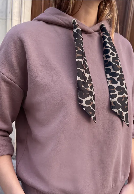 Person trägt rosa Kapuzenpullover mit Leopardenmuster-Kordeln und hochgekrempelten Ärmeln.