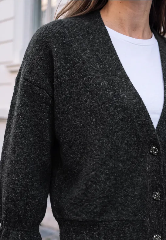 Une femme porte un gilet gris foncé sur un t-shirt blanc.