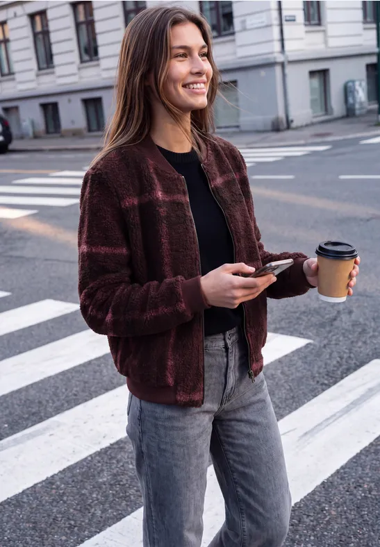 Frau mit Kaffee und Smartphone geht lächelnd über eine Straße.