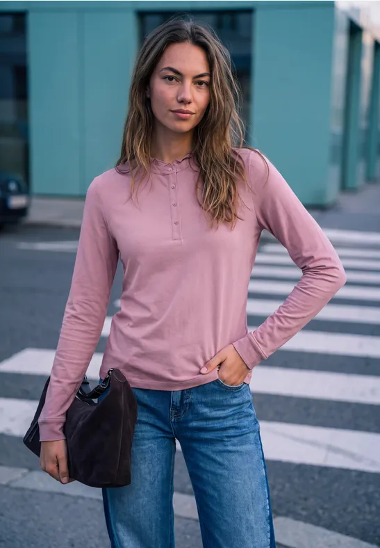 Junge Frau in rosa Langarmshirt und Jeans steht lässig auf dem Zebrastreifen, hält eine Tasche.