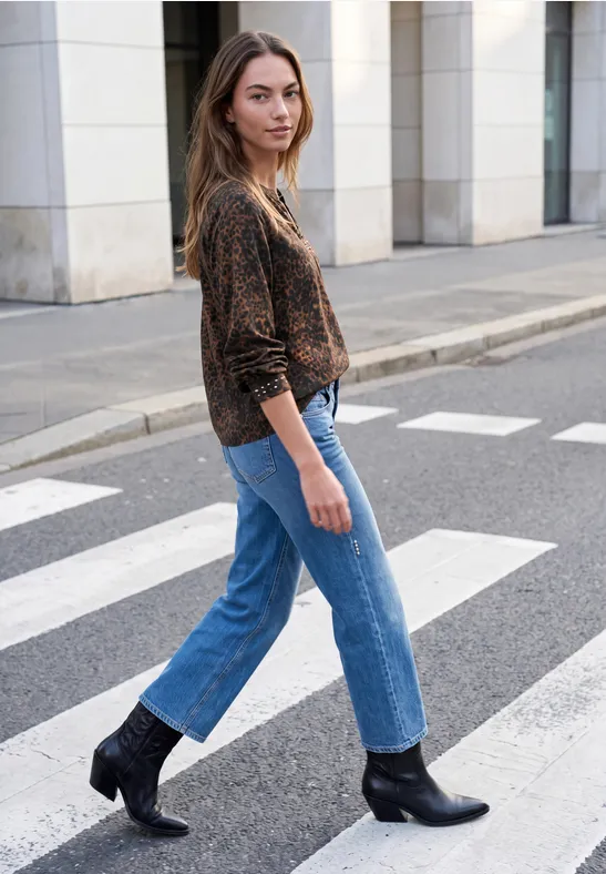 Une femme en pull imprimé, jean et bottines noires traverse un passage piétons.