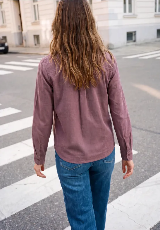 Person mit kastanienbraunem Hemd und blauen Jeans überquert eine Straße am Zebrastreifen