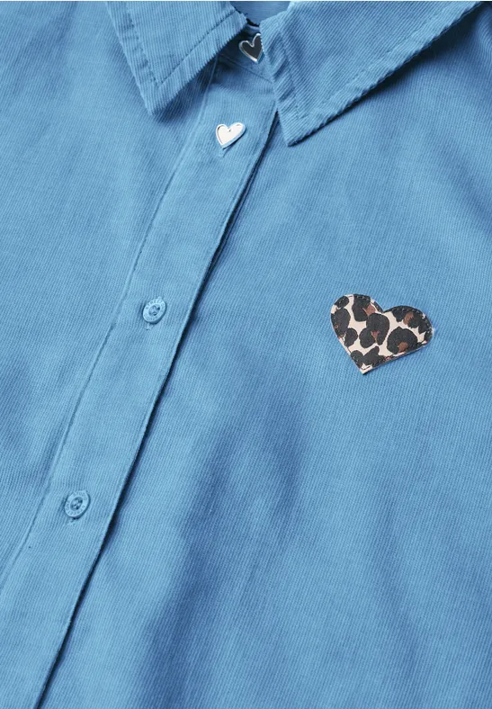 Blaues Hemd mit zwei Herz-Details: weißer Herzknopf am Kragen und Leopardenmuster-Herzpatch auf der Brust.