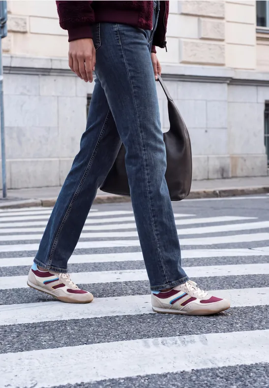 Person in Jeans und Sneakern überquert einen Zebrastreifen auf der Straße.