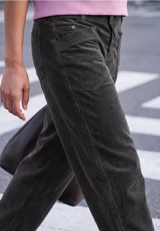 Une personne porte un pantalon en velours côtelé noir en traversant la route.