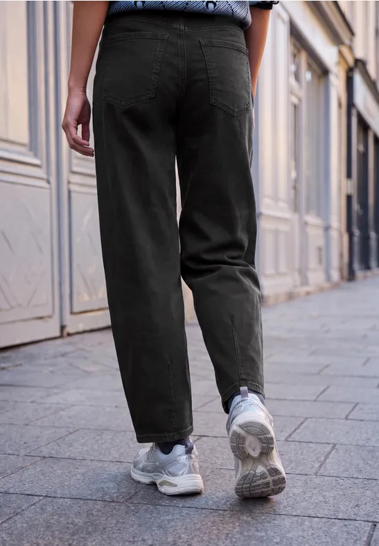 Person mit schwarzer Hose und weißen Sneakern läuft auf einem städtischen Gehweg.