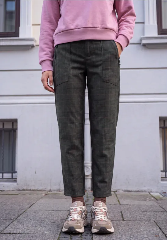 Person steht auf Bürgersteig, trägt grüne Cargohose, rosa Pullover und weiße Sneaker.