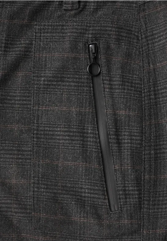 Nahaufnahme eines grauen, karierten Stoffes mit Reißverschluss-Tasche und rundem Zipperanhänger.