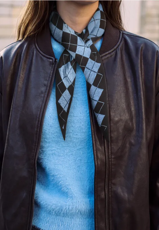 Veste en cuir noir sur un pull bleu clair, foulard à carreaux noir et bleu ciel noué au cou.