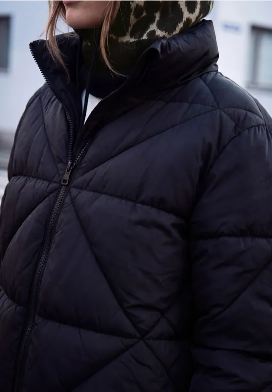 Eine Person trägt eine schwarze, gesteppte Daunenjacke mit hohem Kragen und Leopardenmuster-Stirnband.