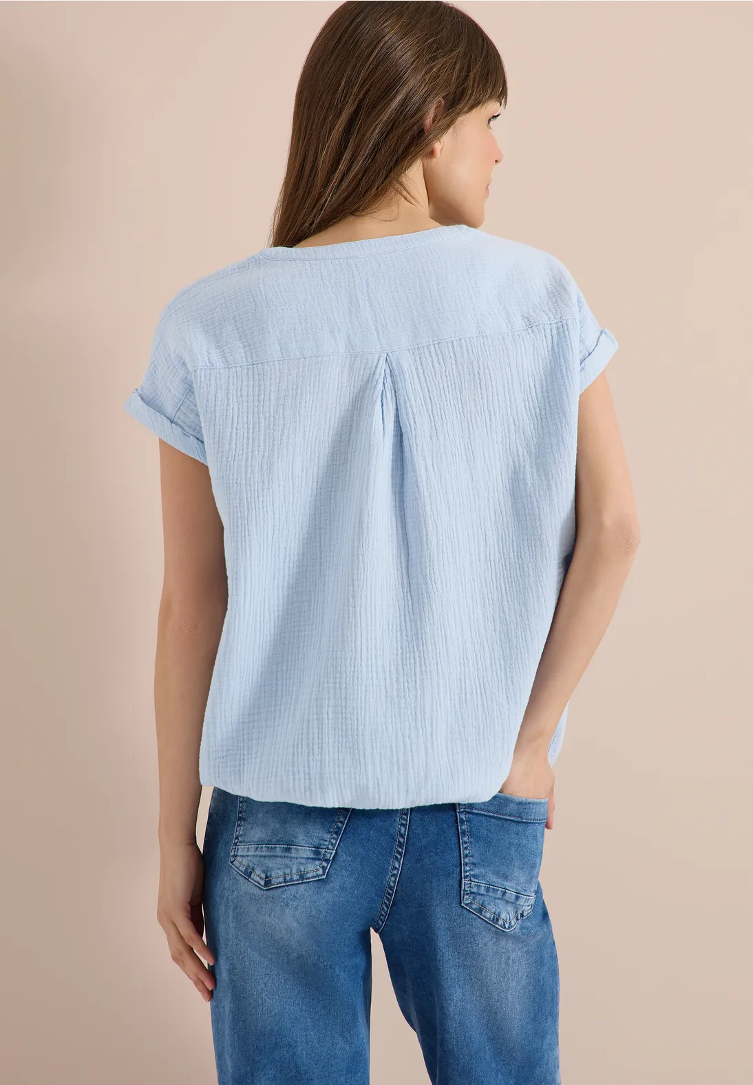 Frau steht von hinten in hellblauem kurzärmligem Oberteil und Jeans.