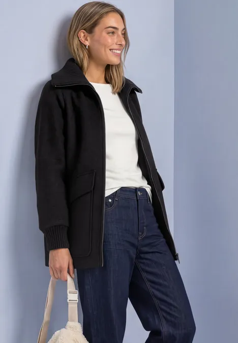 Mantel mit Wollanteil und Strickkragen Black Frau in schwarzer Kapuzenjacke, weißem Shirt und Jeans mit beiger Tasche.