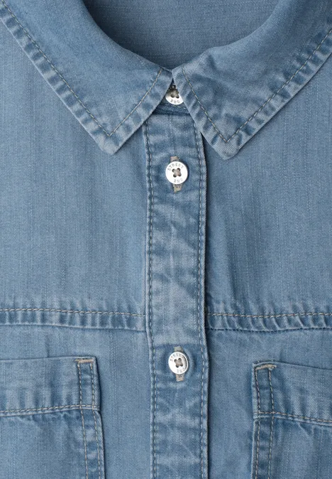 Close-up van een blauwe spijkerjas met metalen knopen en borstzakken.