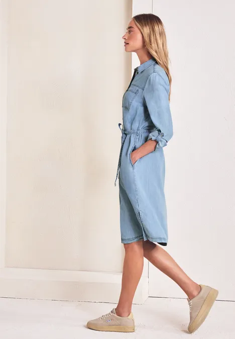 Zijaanzicht van een vrouw in een lichtblauwe denim jumpsuit met ceintuur en plateauzolen.