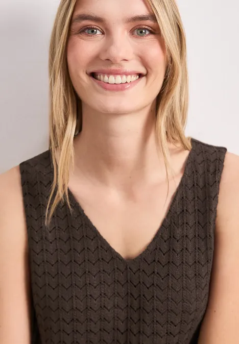 Vrouw met halflang blond haar in een mouwloos zwart kanten top.