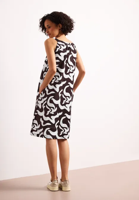 Frau von hinten im schwarz-weiß gemusterten, ärmellosen Midikleid mit Taschen und beigen Sneakern.