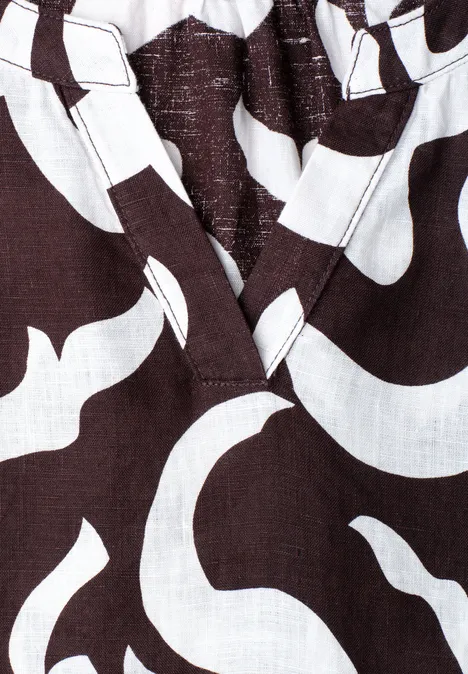 Nahaufnahme eines dunkelbraunen Stoffes mit weißen, geschwungenen Mustern und V-Ausschnitt.