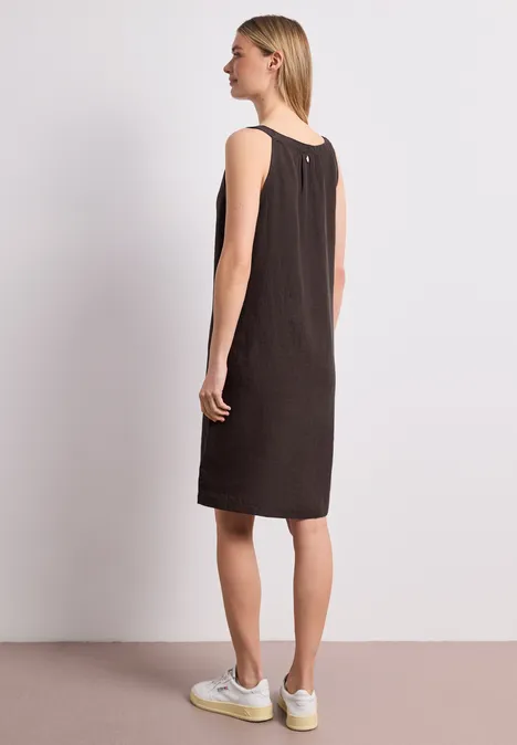 Femme de profil portant une robe marron sans manches et des baskets blanches.