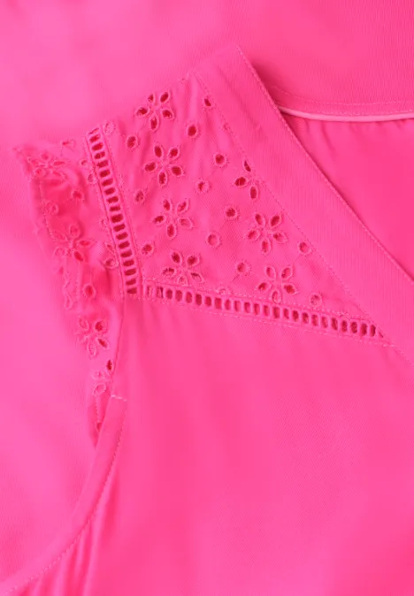 Nahaufnahme eines pinkfarbenen ärmellosen Oberteils mit zarter Lochstickerei an den Schultern.