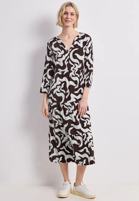 Frau trägt ein knöchellanges Kleid mit abstraktem Schwarz-Weiß-Print und weißen Sneakers.