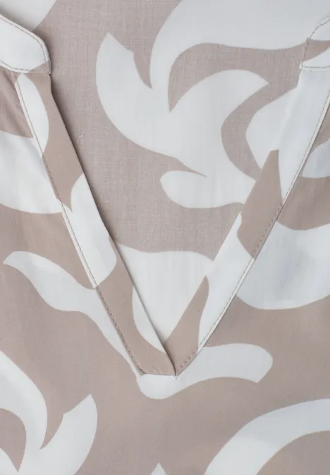 Blusenausschnitt mit V-Form auf beigem Stoff mit weißen, abstrakten Blattmustern.