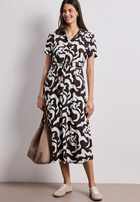 Femme en robe midi à motif abstrait noir et blanc, encolure en V, baskets blanches et sac.