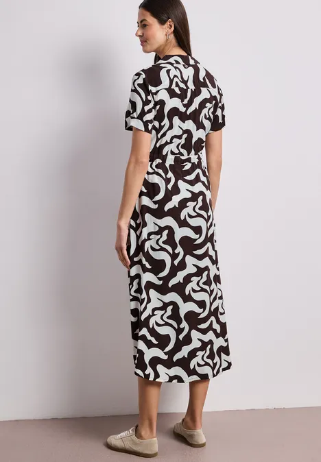 Femme en robe midi à motifs noir et blanc, vue de profil.