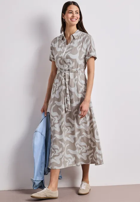 Femme en robe chemise midi à motif abstrait, ceinturée, tenant une veste en jean bleu clair