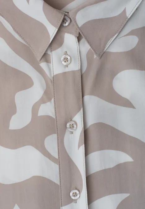 Gros plan d’une chemise avec motif abstrait beige et blanc, boutons apparents et col net.