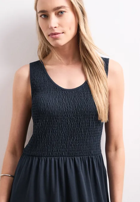 Frau in ärmellosem, schwarzem Kleid mit gerafftem Oberteil und weitem Rock