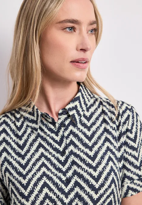 Femme blonde portant un polo à manches courtes blanc et bleu à motif zigzag.