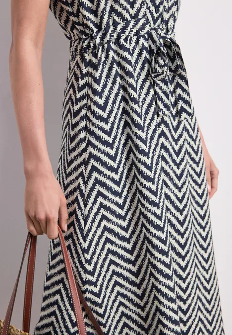 Robe midi noir et blanc à motif zigzag, ceinturée à la taille, tenue par une main.