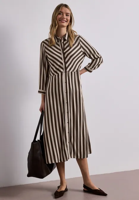 Frau trägt midi Hemdkleid in Schwarz-Beige-Streifen, mit schwarzer Tasche und schwarzen flachen Schuhen.