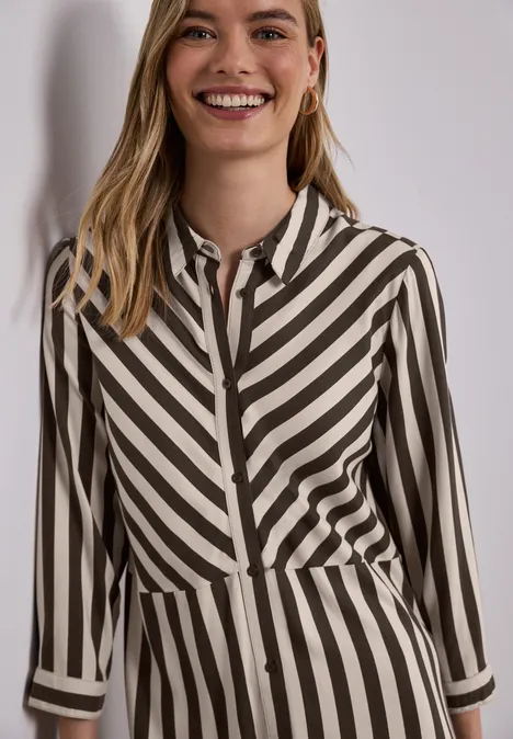 Eine Frau trägt eine Hemdbluse mit diagonalen schwarz-beigen Streifen.
