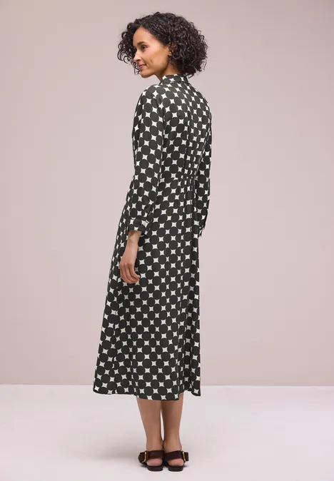 Frau in schwarzem Midikleid mit weißen Punkten, seitlich gewandt, schwarze Sandaletten