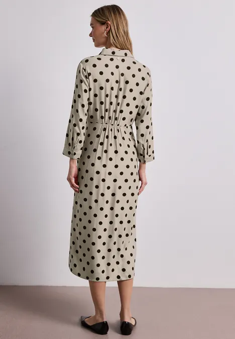 Vrouw van achter in een beige midi-jurk met zwarte stippen, 3/4-mouwen en platte schoenen
