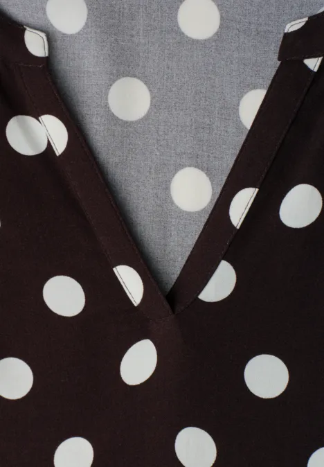 Dunkelbrauner Stoff mit weißen Polka-Dots und V-Ausschnitt, graues Futter mit Punkten.