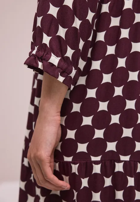 Gros plan sur une main et un bras vêtus d'une robe ample à motifs de cercles blancs sur tissu rouge sombre.