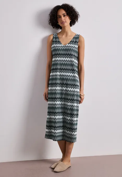 Une personne porte une robe midi sans manches à motif zigzag et des espadrilles plates.