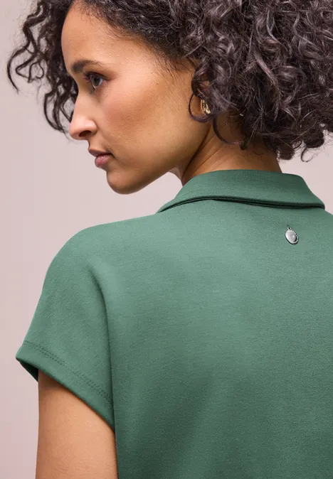 Vue de dos d'une personne aux cheveux bouclés portant un polo vert.