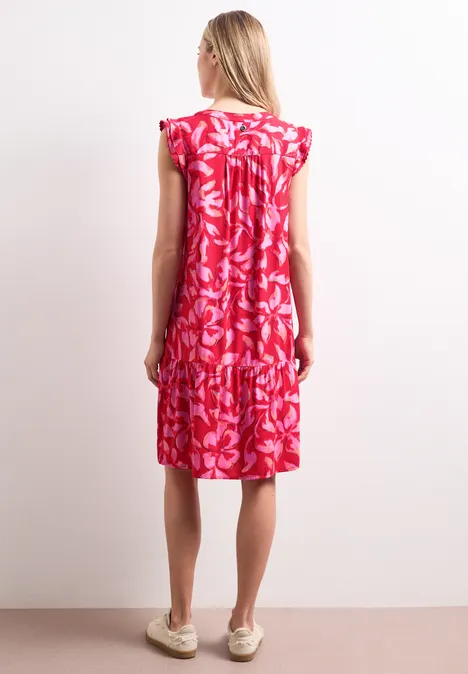 Frau von hinten in einem knielangen, roten Kleid mit weißem Blumenmuster und flachen Sommerschuhen.