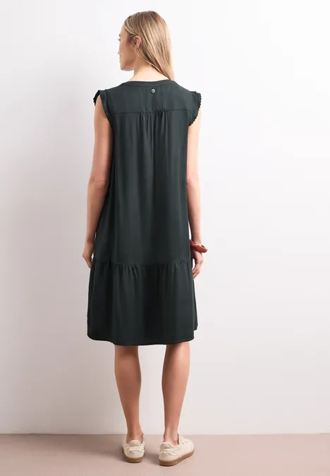 Frau von hinten in knielangem schwarzen Kleid mit kurzen Ärmeln und Rüschen.