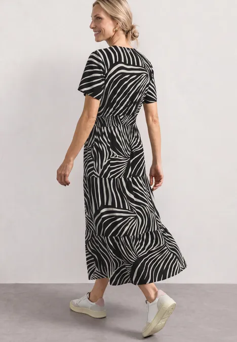 Frau in midilangen Kleid mit schwarz-weißem Zebramuster und kurzen Ärmeln, weiße Sneaker.