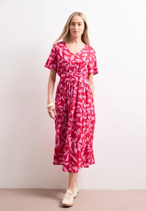 Robe midi avec imprimé et détail smocké salsa red Une femme porte une robe midi rouge imprimée et pose devant un mur clair minimaliste.