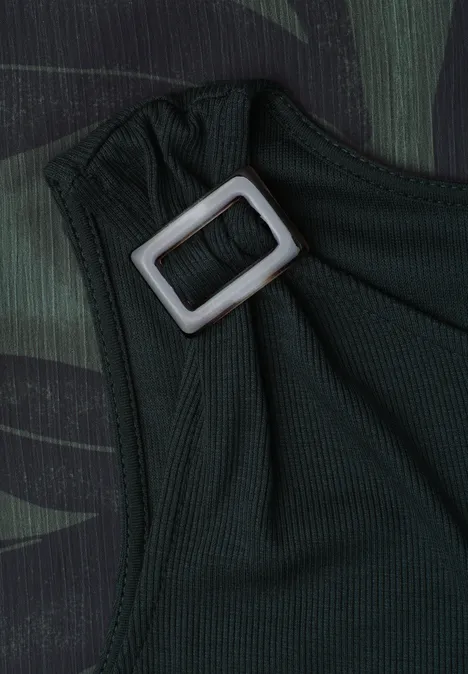 Detailaufnahme eines dunkelgrünen Stoffs mit verstellbarem, silbernem Rechteckverschluss auf Camouflage-Hintergrund.