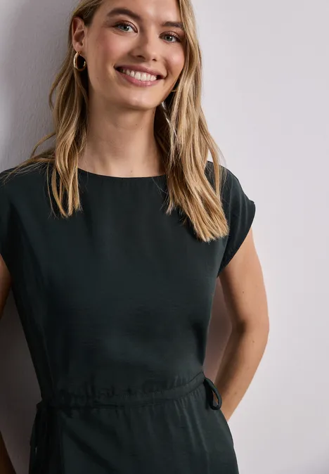 Eine Frau in einem schlichten, dunkelgrauen Kleid mit Gürtel, Cap-Sleeves und hohem Rundhalsausschnitt