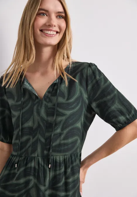 Frau in dunkelgrünem Midikleid mit Blattmuster, halblangen Ärmeln und V-Ausschnitt.